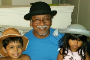 Ravi smiling in the center with his children Quinn and Priya when they were young, they are all wearing fancy hats